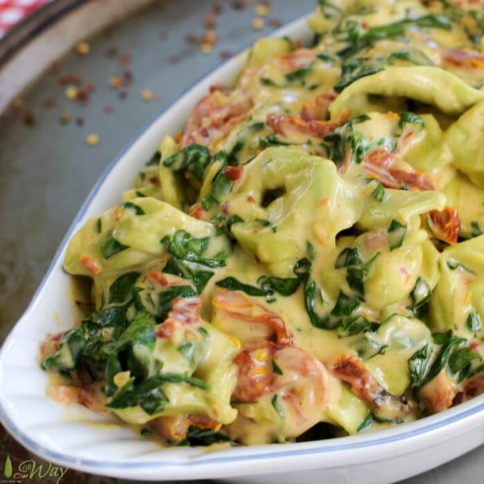 Spinach tortellini with strip of red sun-dried tomatoes and baby spinach in a rich creamy parmesan sauce in a oval white gratin dish. 