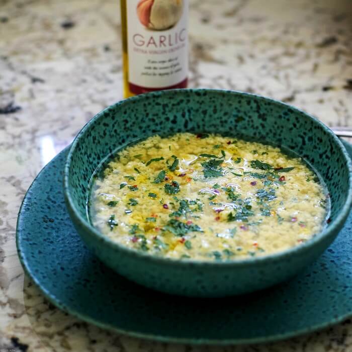 egg drop soup in a turquoise and black speckled bowl on top of matching plate with blue, green, brown plaid tea towel. 