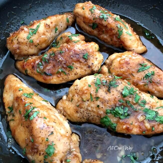 Six browned chicken tenders in a non-stick skillet with honey garlic sauce surrounding the chicken. 