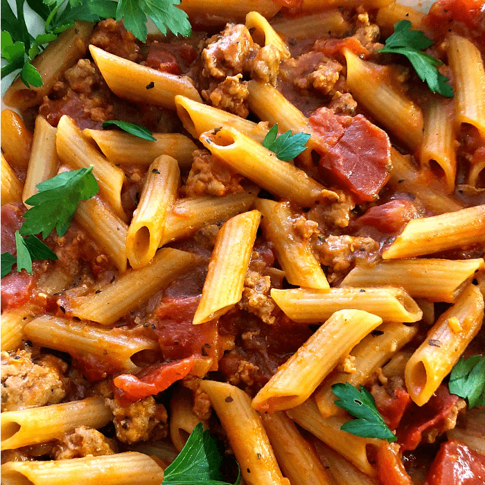 Penne pasta covered with tomato sauce and Italian sausage chunks with a sprinkle of Flat-leaf parsley