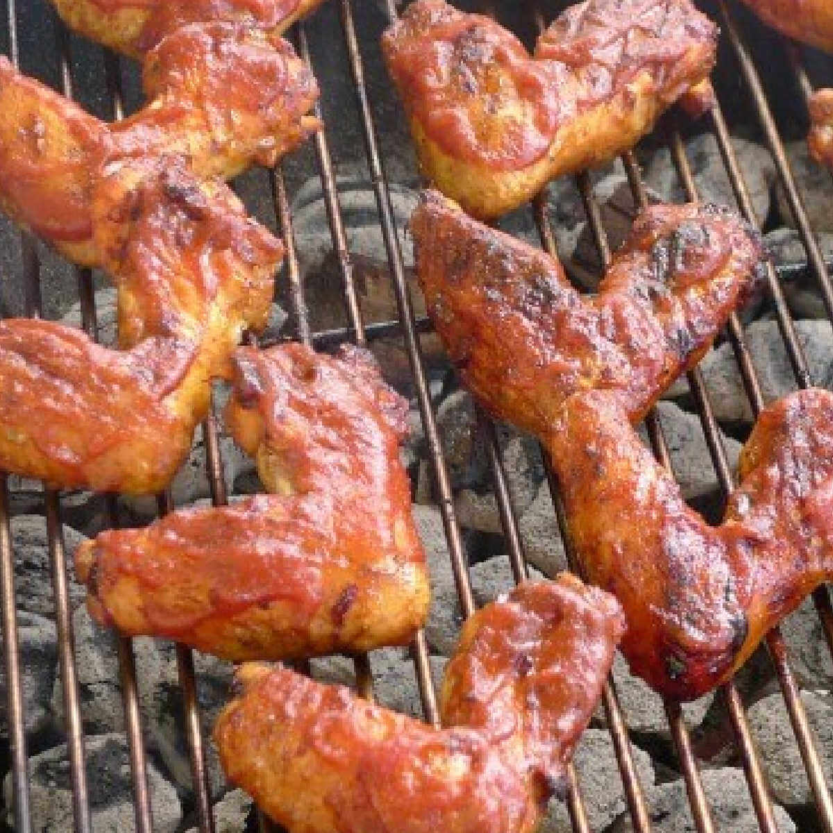 Close up of barbecued chicken on round grill grate cooking.