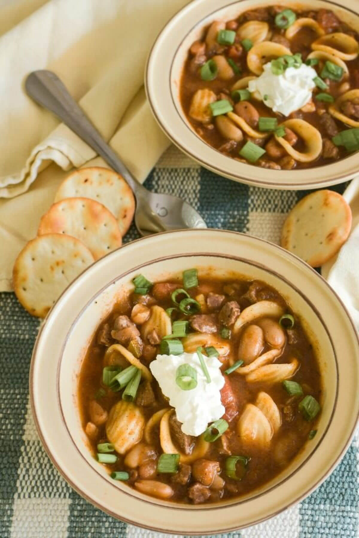 Two bowls of Meaty chili in bowls with pasta and a sprinkle of chopped green onions. 