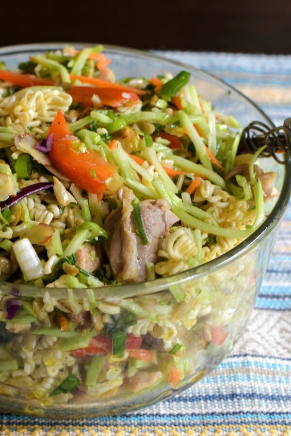 A closeup of a clear glass bowl filled with Ramen Broccoli Slaw Recipe with red pepper matchsticks and chicken pieces top.