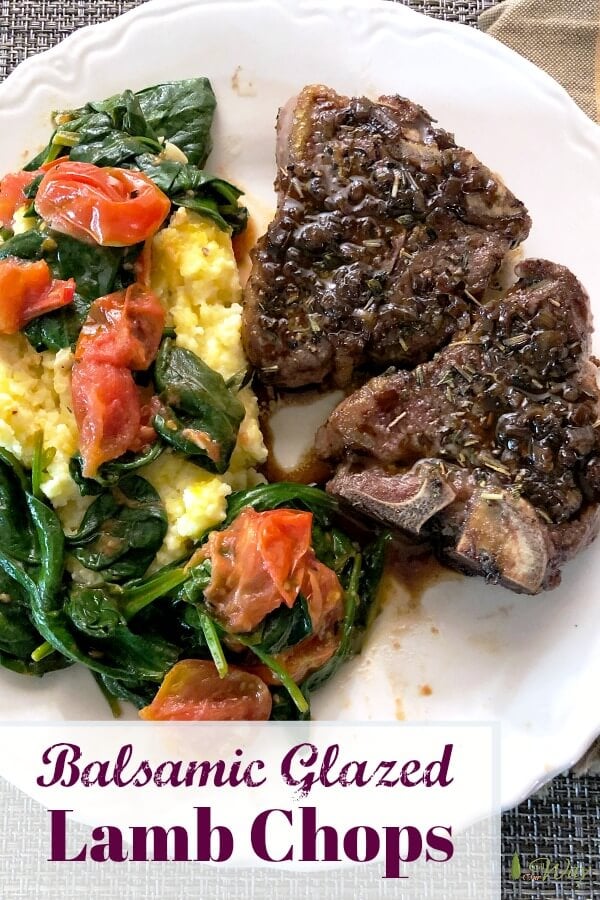 Two browned lamb chops on a white plate with yellow polenta covered with sauteed red grape tomatoes and green baby spinach.