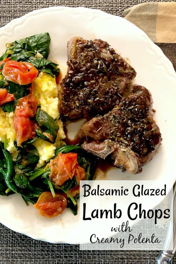 Two lambchops, yellow polenta, grape tomatoes, and baby spinach on a white plate. 