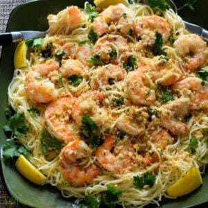 Easy shrimp scampi on top of angel hair pasta with slivers on lemon on a deep green square platter.