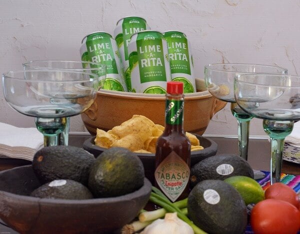 Snack table with avocados, green margarita glasses, TABASCO® Sauce, green and white aluminum cans chilling in a brown pottery bowl of ice. 