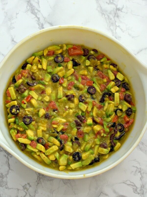 A large white bowl filled with Italian avocado salsa with the addition of tomatoes, black olives, green chilies and onions. 