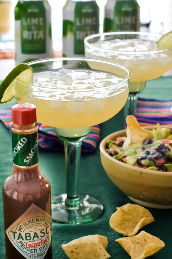 Two green margarita glasses filled with Lime-A-Ritas over ice with avocado salsa in a tan pottery bowl with a bottle of TABASCO® Chipotle Sauce next to the drinks.