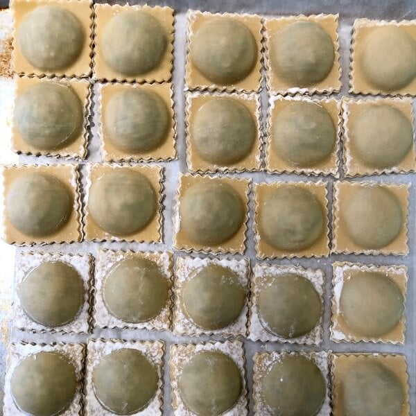 A parchment lined baking sheet filled with rows of lamb ravioli. 
