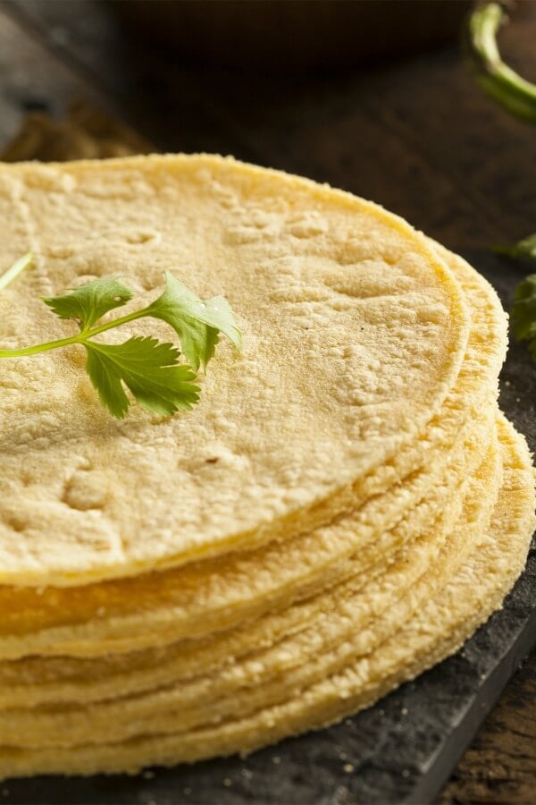 Stack of corn tortillas on a dark table with a green cilantro stem on top. 