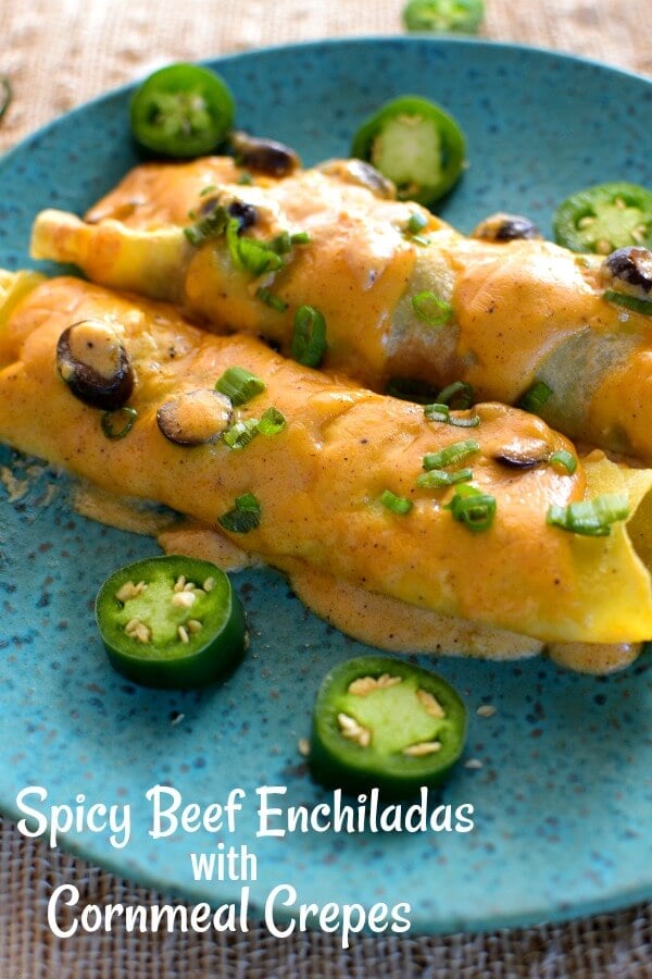 Two cheese covered beef enchiladas on an aqua speckled pottery plate with slices of jalapeños surrounding the enchiladas. 