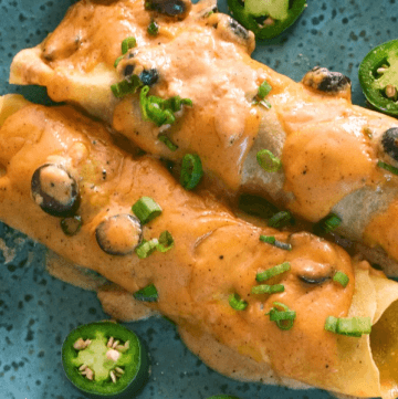 Two ground beef enchiladas covered in cheese sauce and garnished with black olives, green onions and jalapeños.