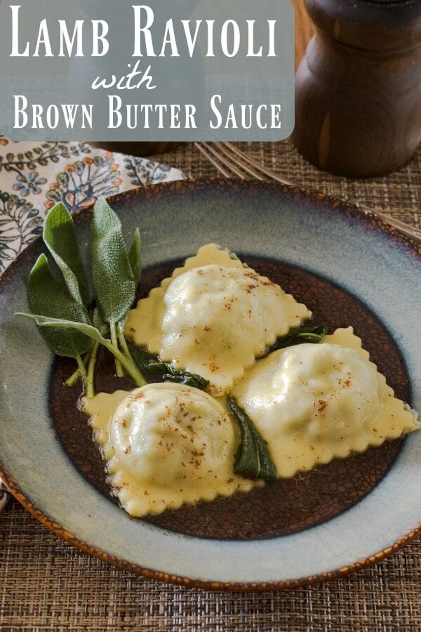 Three lamb ravioli on a blue and brown round plate with a sprig of sage on the side. A multi-color napkin is under the plate.