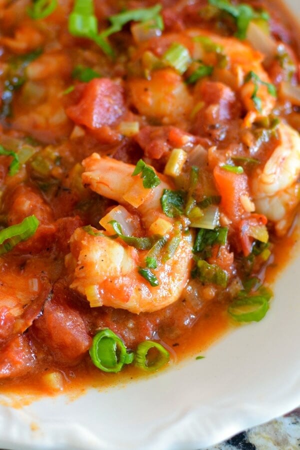 A close up of pink shrimp in a rich tomato sauce sprinkled with green onions and parsley. 
