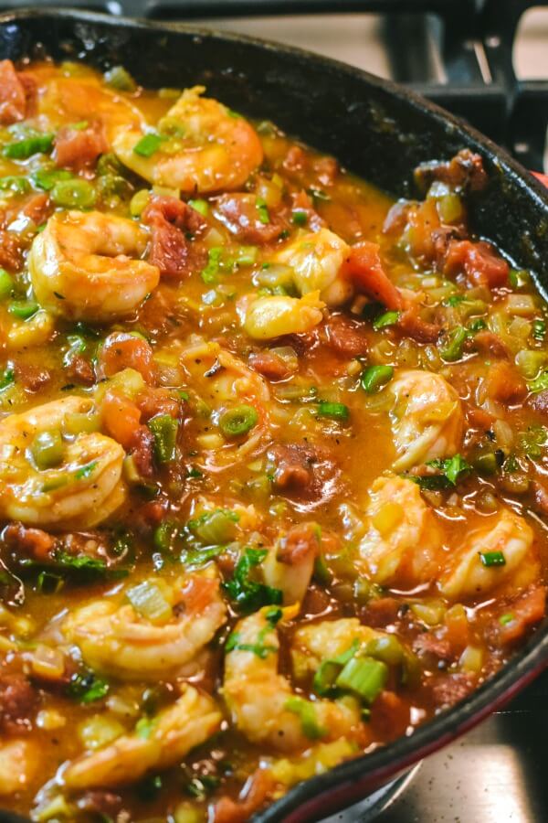 On top of a stove burner a cast iron pan filled with a tomato mixture with shrimp.