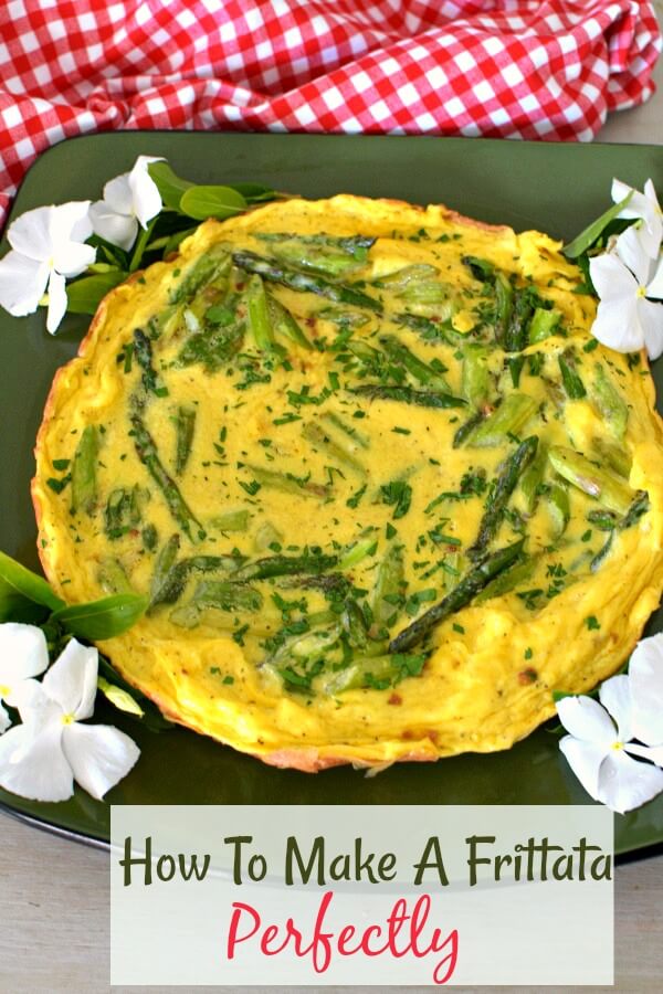 An asparagus frittata on a green platter with four white flowers at each corner. Red and White checked towel and the top. 