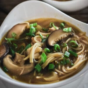 Two triangular white bowls filled with hot and sour soup and sprinkled with green onion rings.