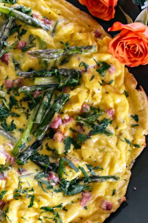 Asparagus frittata on a green platter with a coral rose flowers on the upper right. 