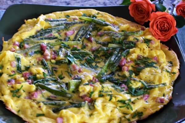 Close up of an asparagus frittata on a green plate with a coral rose at the edge of the plate.