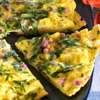Close up of an asparagus frittata on a green plate with a slice cut. Coral roses on the right side.