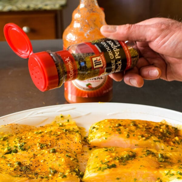 Four Halibut fillets being seasoned with McCormick® Black Pepper with Frank's®RedHot Sauce in the background. 