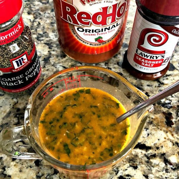 A measuring cup full of the citrus herb marinade for the grilled halibut on a marble counter. A container of pepper, hot sauce, and seasoned salt in the background. 