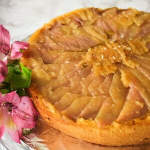 Golden pear round upside down cake with fuchsia lilies on the side of the cake plate.