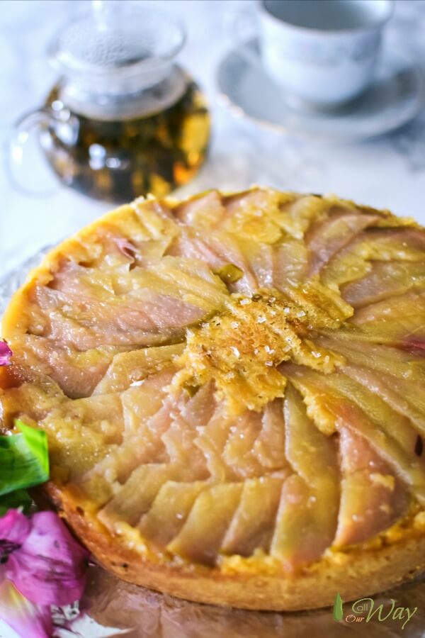 Upside down pear polenta cake with a carafe of tea and a tea cup . 