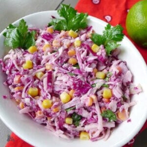 Purple coleslaw and yellow corn with cilantro in a white bowl on rustic wood boards.