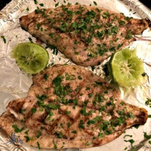 Two Florida Pompano fillets that are grilled on a tray, seasoned with lime and parsley.