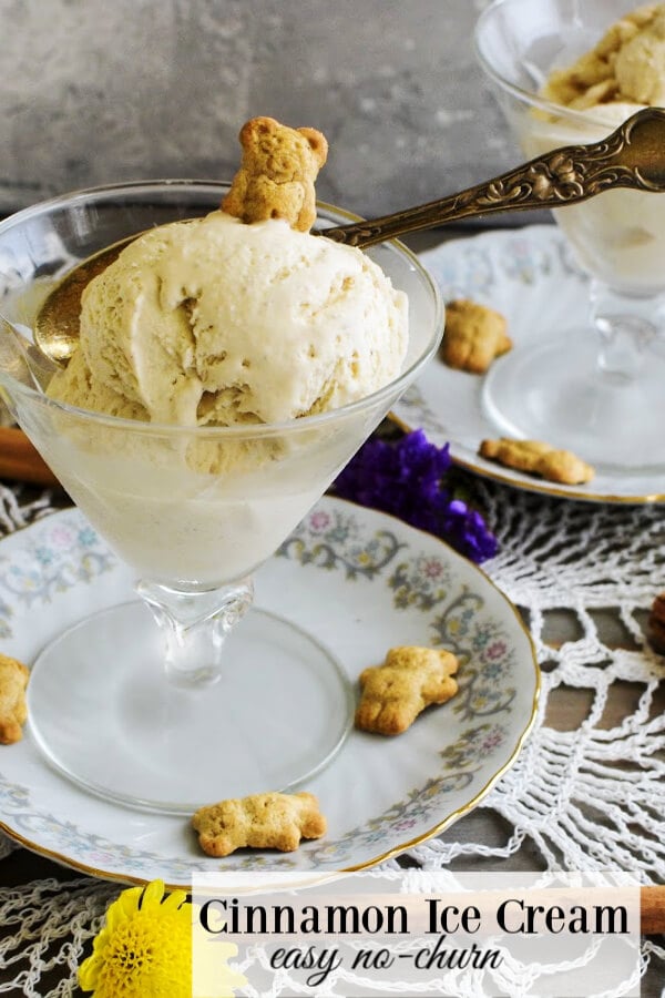 Glass goblet with cinnamon ice cream a teddy bear cookie on top and silver spoon stuck in the dessert all on a china flower rimmed plate. More teddy bear cookies on plate and yellow and purple flower buds on lace doily. 