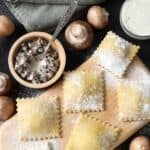 Fresh pasta filled with three kinds of mushroom are placed on a wooden cutting board.