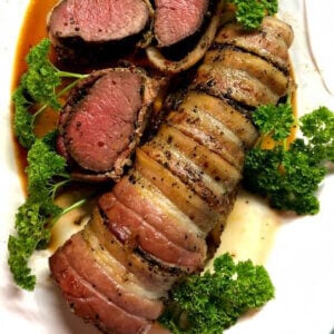 Grilled antelope tenderloin wrapped in bacon and sliced on a white platter.