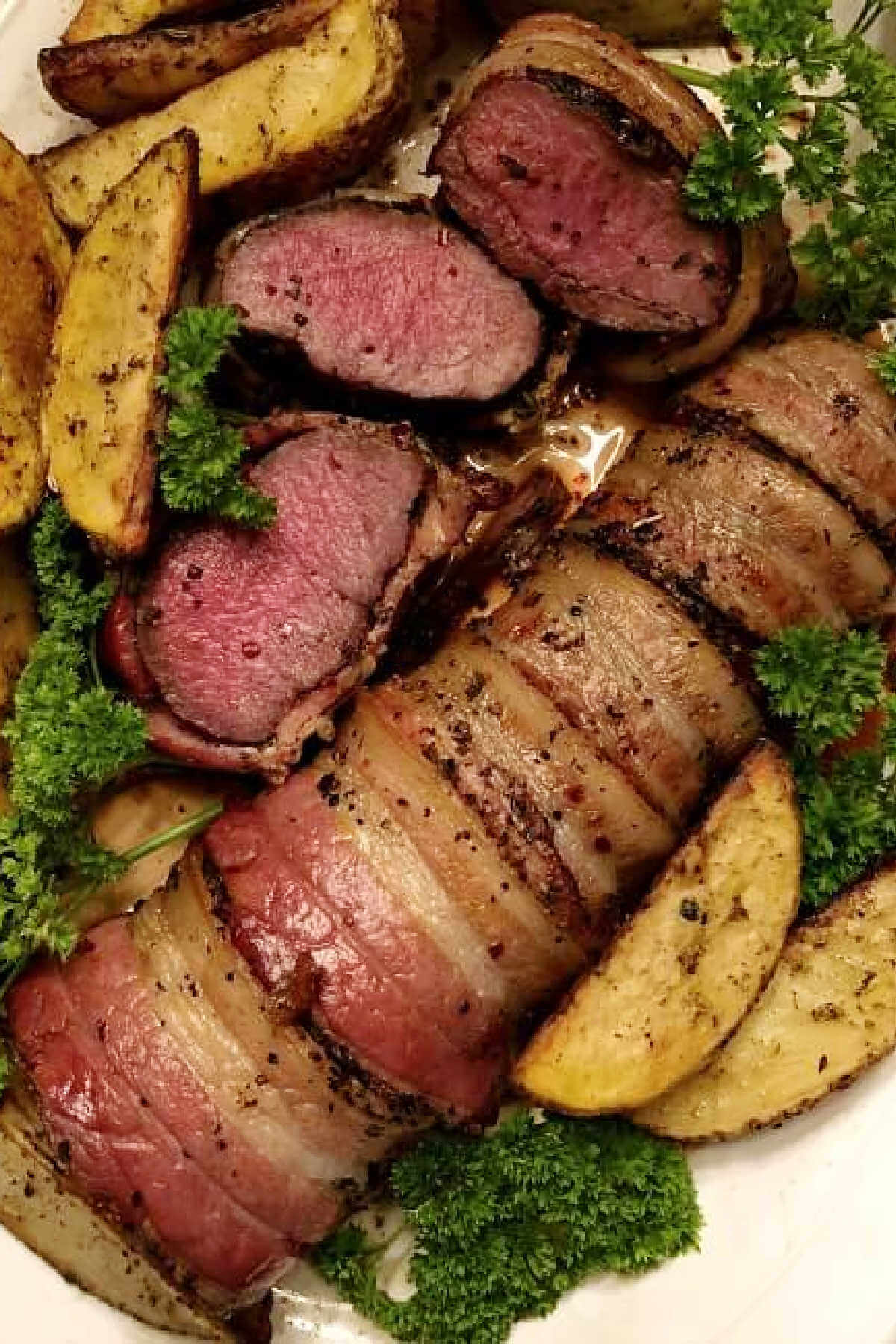 Grilled antelope tenderloin wrapped in bacon on plate with baked potato wedges and parsley. 