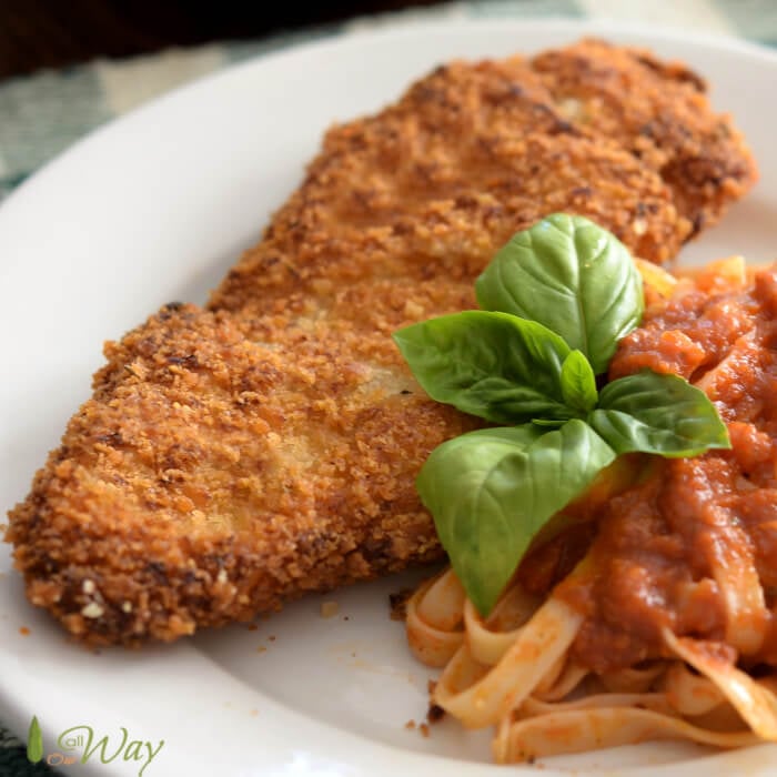 Golden Brown Chicken Milanese with a side of pasta and tomato sauce, spring of basil on the white plate. 