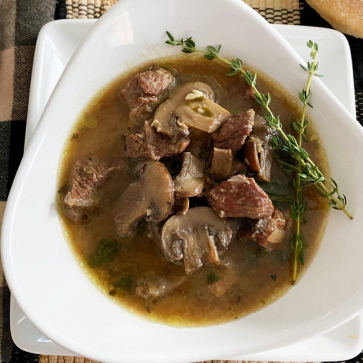 Mushroom Steak Soup in a White bowl with spring of fresh thyme