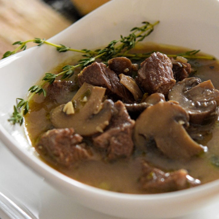 Roasted Mushroom steak soup with chunks of meat and mushrooms in broth in white triangular bowl. 