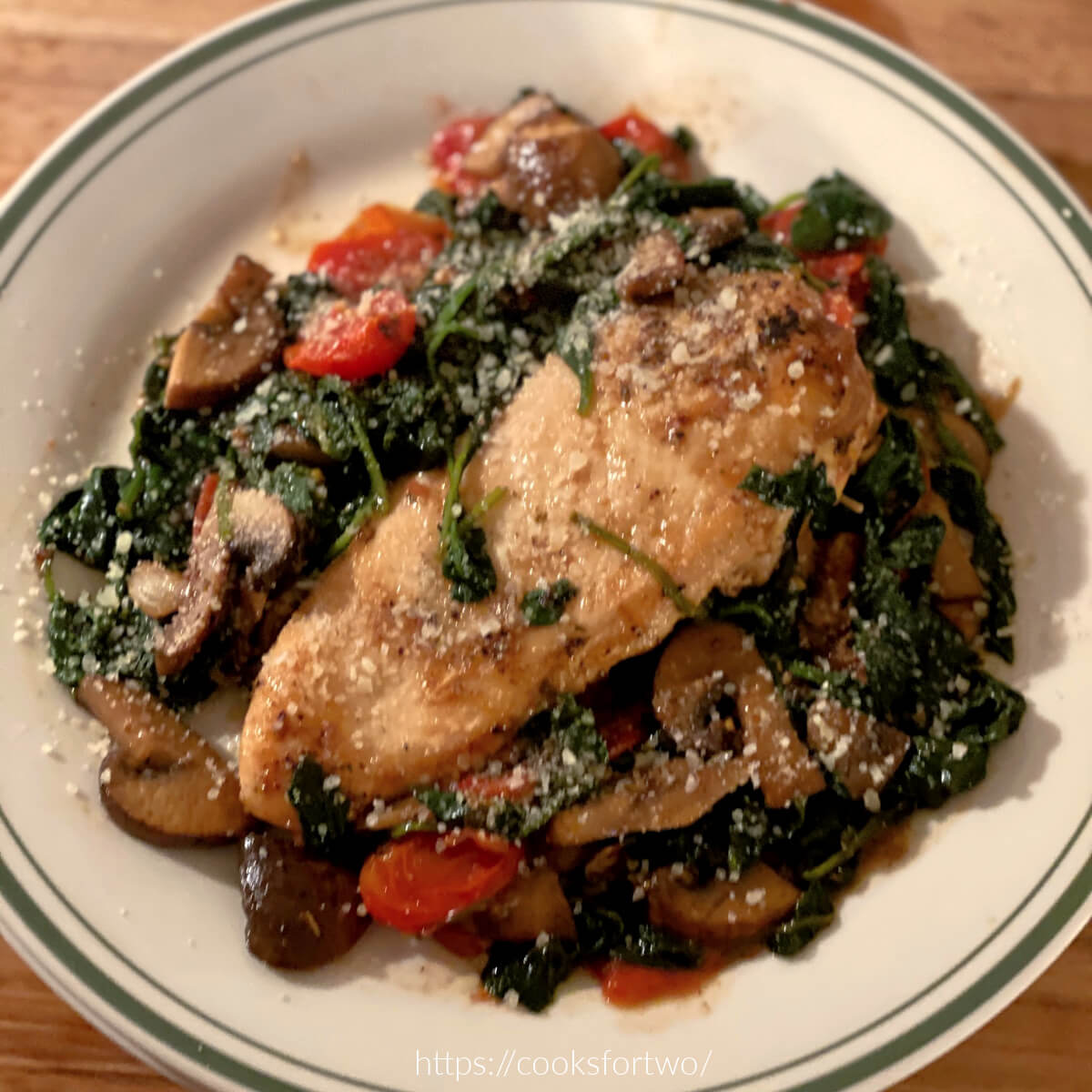 Chicken Florentine on Green edged plate with spinach, tomatoes, and mushroorms.