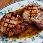 Two grilled pork chops on leaf patterned plate covered with maple glaze.