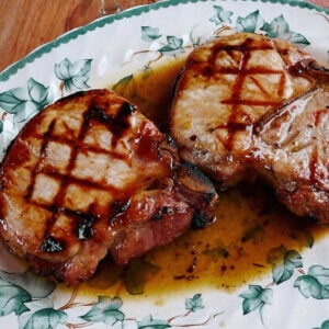 Two grilled pork chops on leaf patterned plate covered with maple glaze.