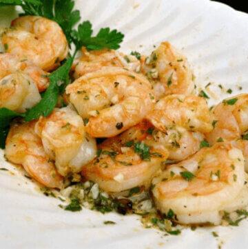 Grilled Shrimp with lemon , garlic and onions in white bowl with parsley.