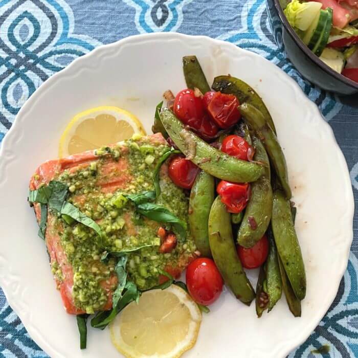 Sugar snap peas on white plate with roasted salmon and sliced lemons