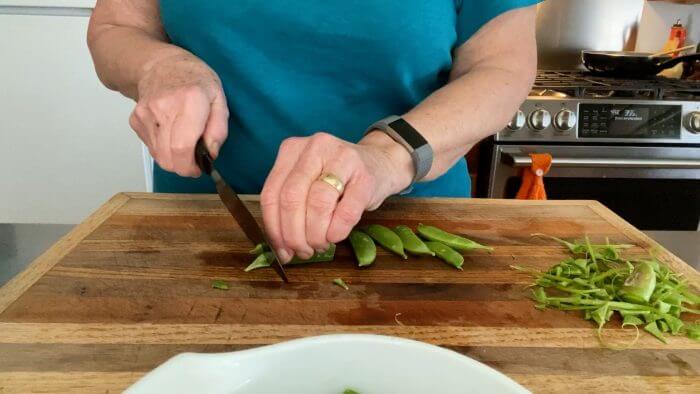 Cutting and trimming sugar snap peas on cutting board. 