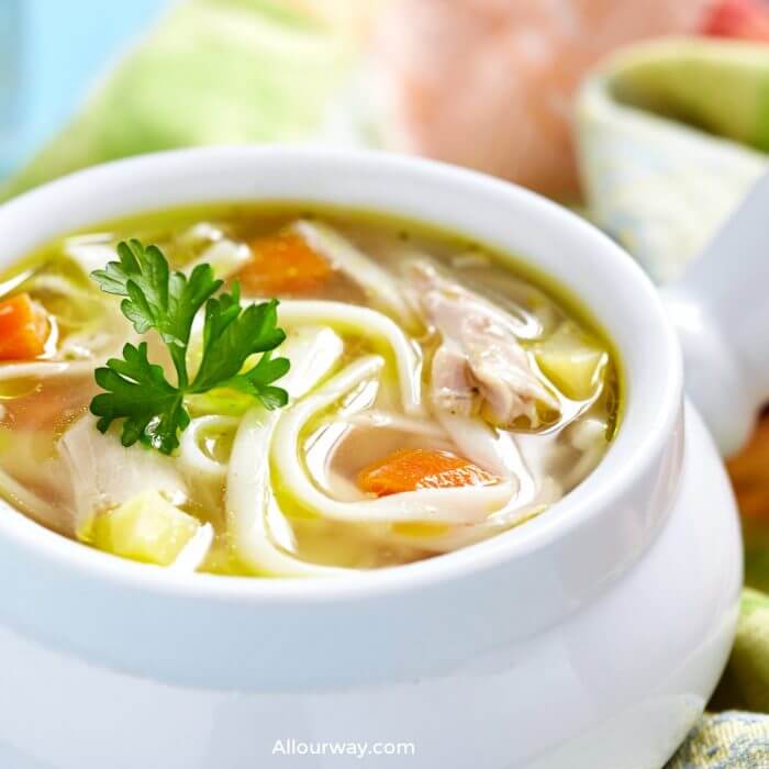 White bowl filled with homemade chicken soup with noodles and carrots and celery. 