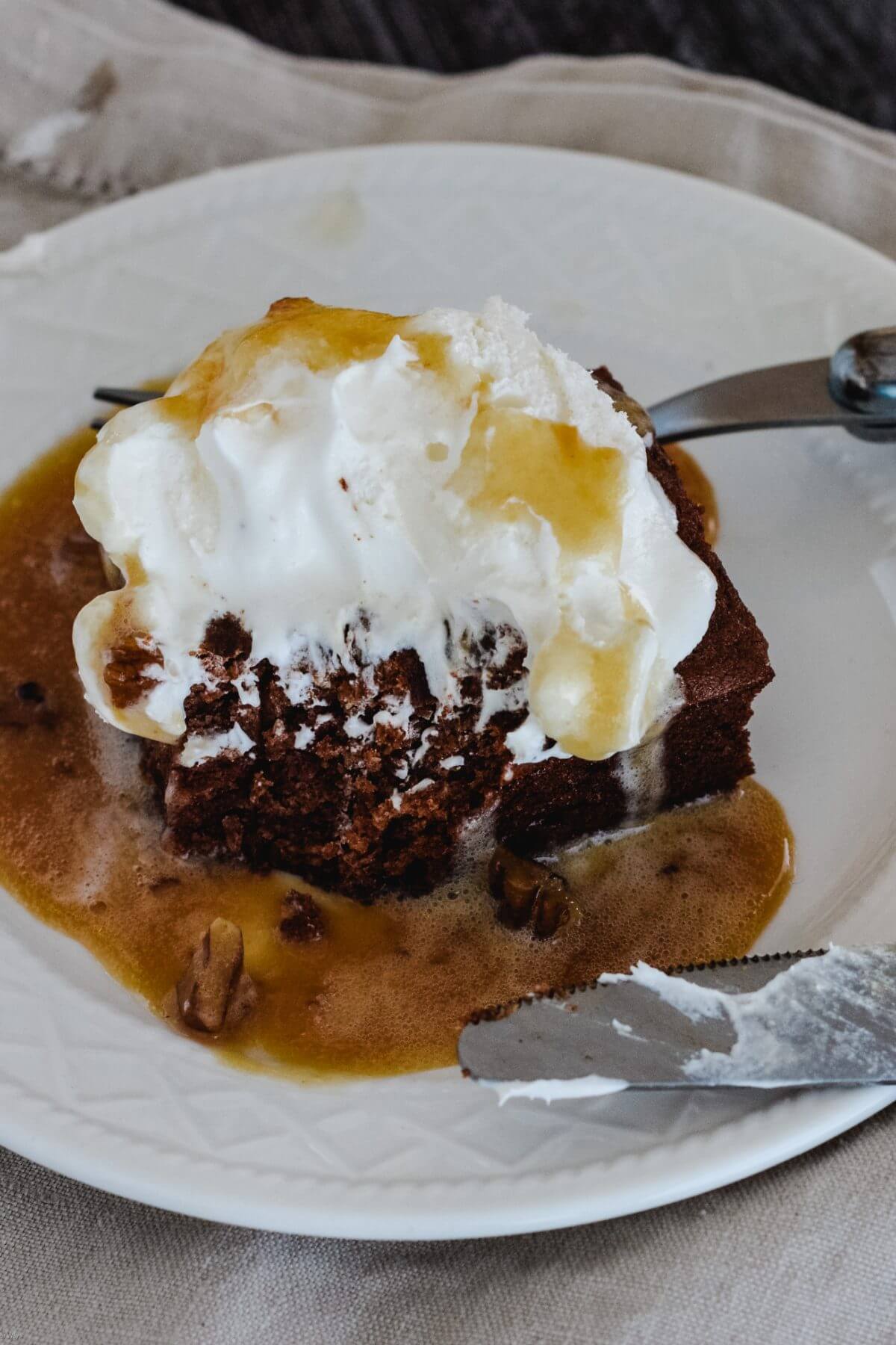 Close-up of persimmon pudding with whipped cream and caramel pecan sauce on white plate with fork. 