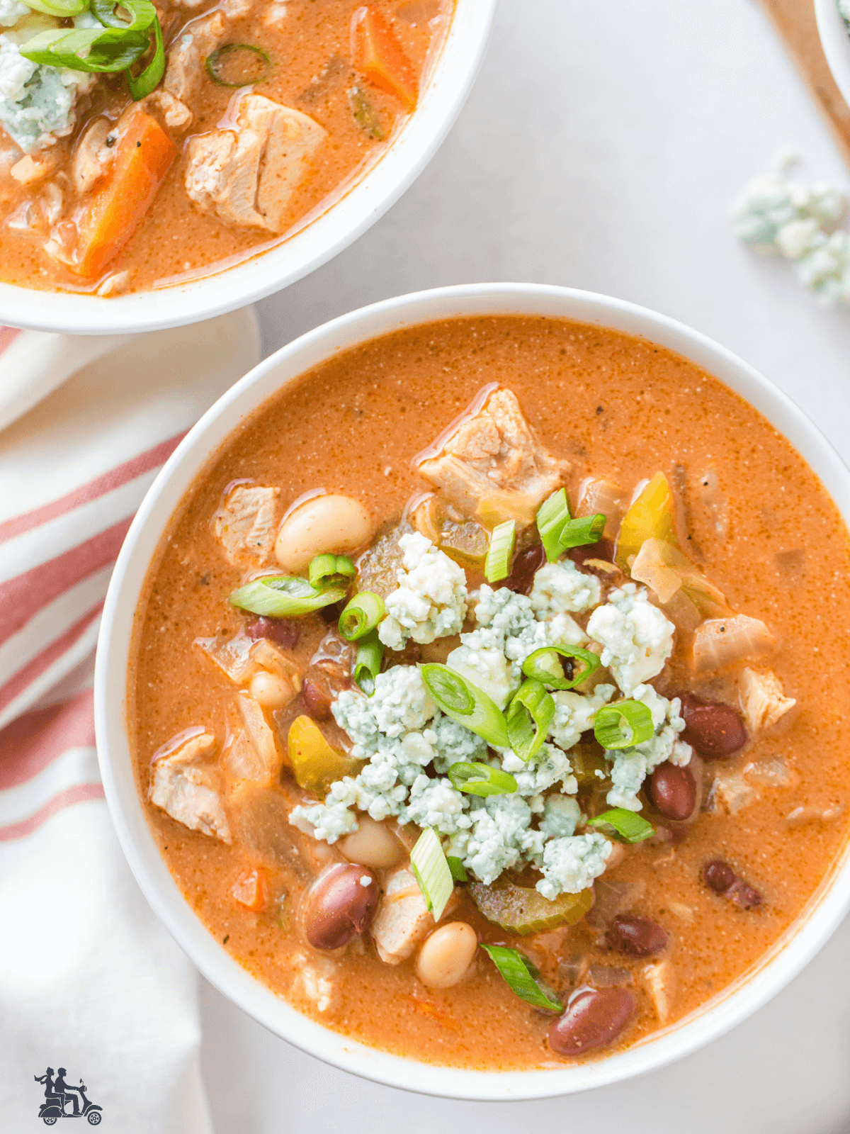 Thick creamy Buffalo Chicken Soup in white bowls and garnished with blue cheese and green onions. 