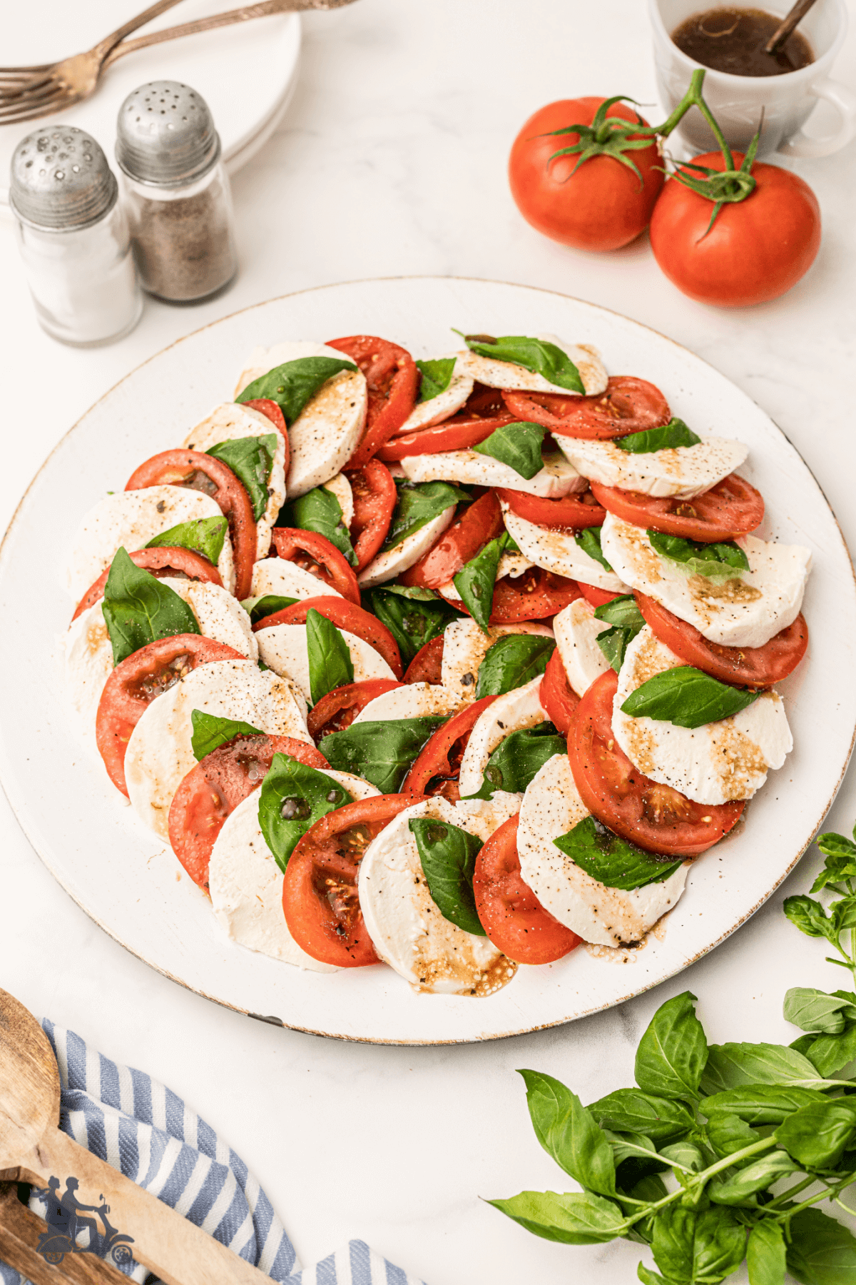 A Caprese Salad on a white platter with the tomatoes, mozzarella, and basil leaves layered in a circle. 