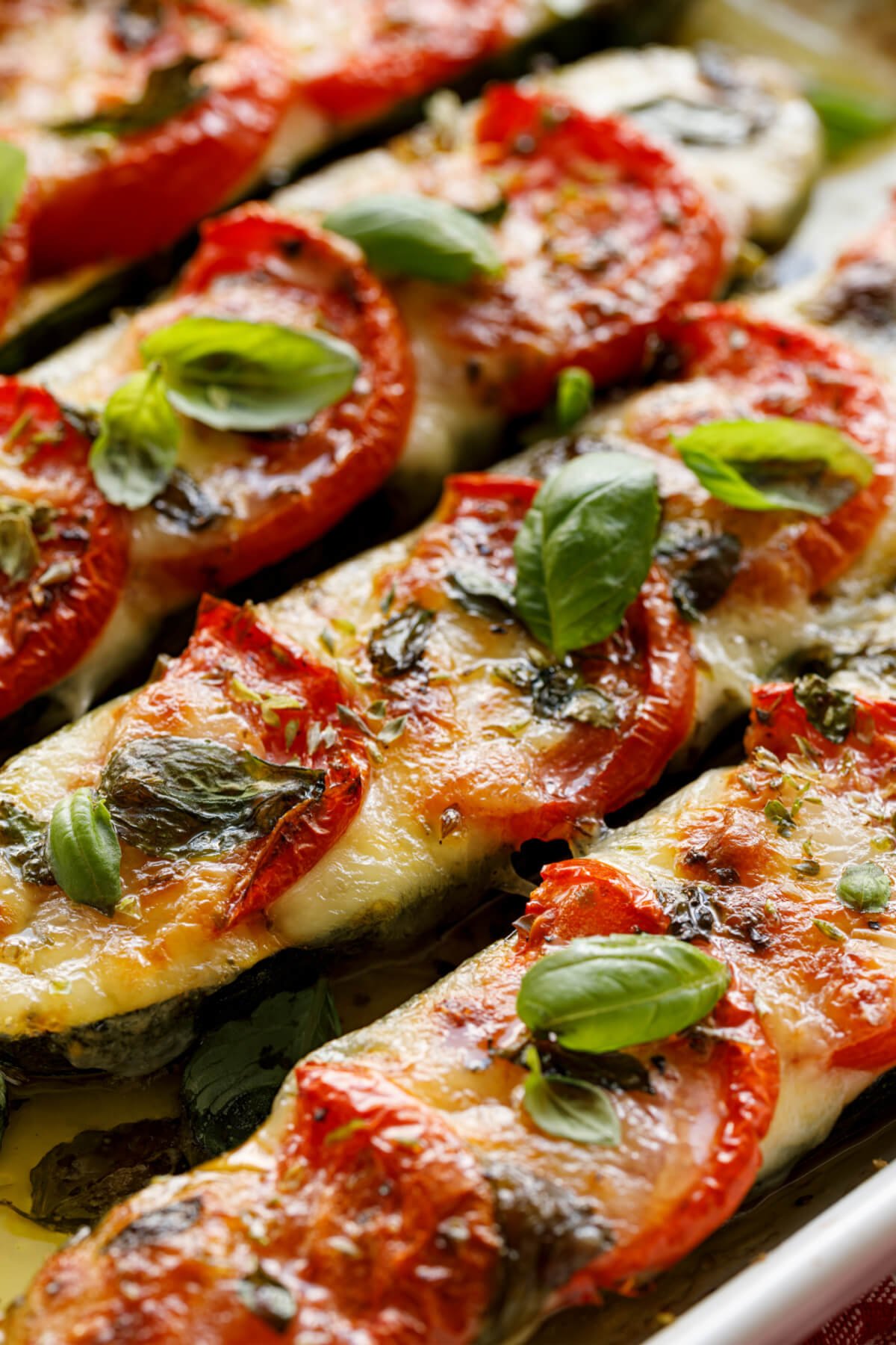 Roasted zucchini boats filled with mozzarella cheese, topped with sliced tomato and fresh herbs.