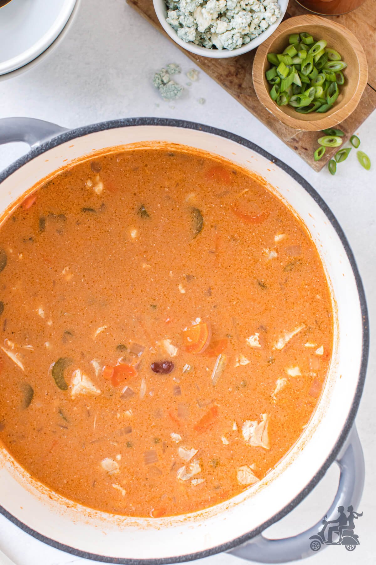 Dutch Oven full of Buffalo chicken Soup Recipe with sliced green onions and bleu cheese on the side. 